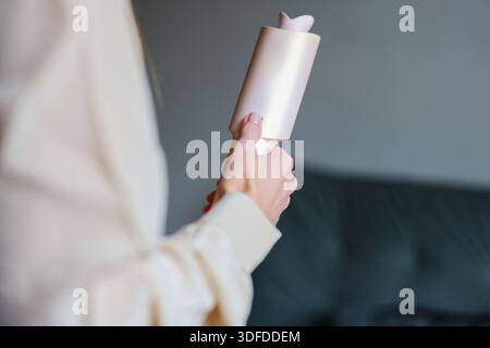 Primo piano di una donna che tiene a casa un moderno strumento per lo styling dei capelli, che rappresenta la routine di bellezza, la cura di sé e lo stile di vita di tutti i giorni Foto Stock