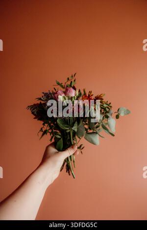 Mano che regge un colorato bouquet floreale su un caldo sfondo pastello Foto Stock