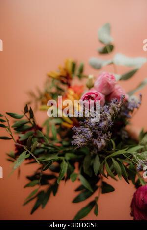 Mano che regge un colorato bouquet floreale su un caldo sfondo pastello Foto Stock