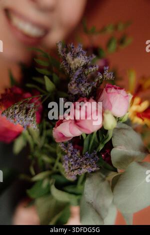 Mano che regge un colorato bouquet floreale su un caldo sfondo pastello Foto Stock