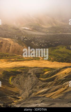 Vista delle colline ondulate dipinte in tonalità ocra, verde e grigio, avvolte da un velo nebbioso che crea un paesaggio etereo, Landmannalaugar, Central Foto Stock