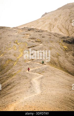 Vista di due escursionisti che attraversano un sentiero tortuoso in cima a un'aspra cresta di montagna tintinnata sotto un cielo tenue, un viaggio nel cuore della bellezza selvaggia, Landmann Foto Stock