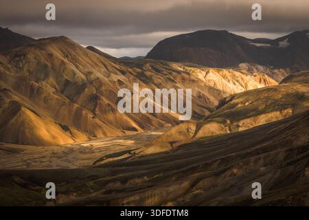 Vista della luce dorata del sole che baciano le aspre montagne multicolore, creando un drammatico gioco di luci e ombre attraverso la vastissima valle, Landmannalaug Foto Stock