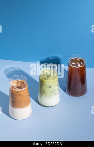 Tre bevande ghiacciate servite in bicchieri trasparenti su uno sfondo pulito e minimalista, tra cui un latte matcha, un caffè ghiacciato e un latte ghiacciato. Foto Stock
