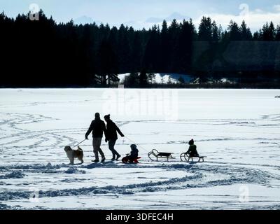 Il 4 gennaio 2026 ad Aitrang, in Germania, le persone camminano attraverso il lago ghiacciato ricoperto di neve e ghiacciato sotto un cielo azzurro, a causa del rischio di ghiaccio e delle condizioni pericolose. Foto Stock