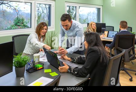 Team aziendale diversificato che collaborano al progetto in un moderno ufficio di coworking situato nella foresta Foto Stock