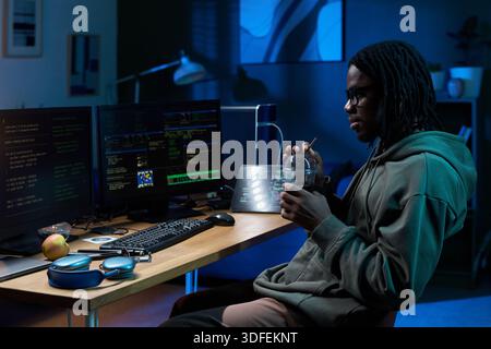 Giovane Black Man che lavora al computer durante l'impostazione Night in Office Foto Stock