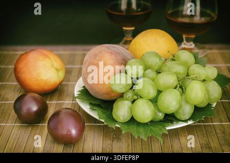Natura morta: Sul tavolo su un piatto ci sono frutta, accanto a due bicchieri di vino Foto Stock