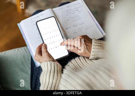 Donna anziana che usa appunti scritti e telefono cellulare Foto Stock