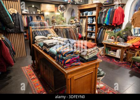 Interno di un negozio vintage di abbigliamento uomo alla moda con vari tipi di vestiti e accessori esposti su appendiabiti e tavoli, abbigliamento elegante esposto in un negozio di seconda mano vecchio stile Foto Stock