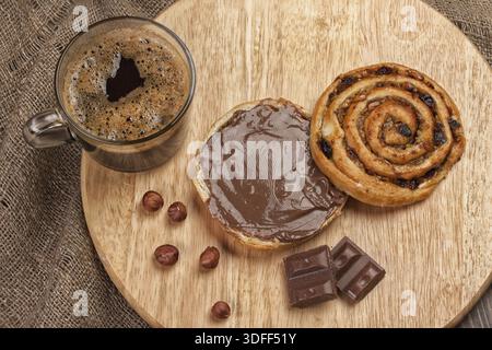 Tazza di caffè, pane, burro e noci su un tavolo di legno Foto Stock