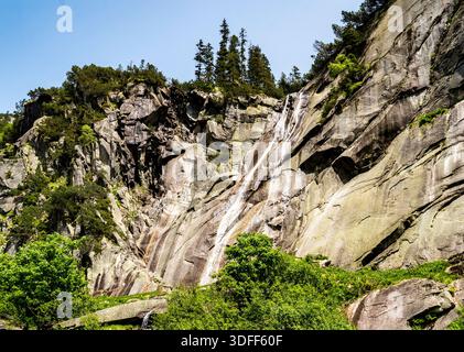 Una cascata panoramica che scende giù da una scogliera rocciosa circondata da vegetazione lussureggiante. Foto Stock