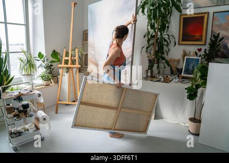 Artista donna creativa che ama l'hobby dell'arte terapeutica presso lo studio di casa, collocando dipinti su cavalletto. Foto Stock