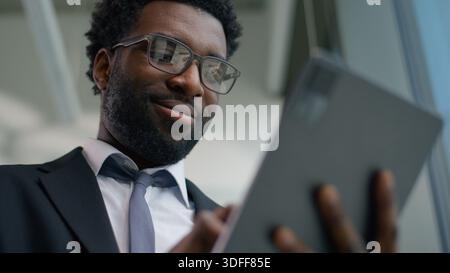 Felice uomo d'affari afroamericano in ufficio sorridente utilizzando un tablet digitale uomo d'affari con tecnologia moderna sorridente manager maschile professionale di successo Foto Stock