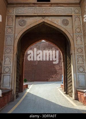 Vista di una porta ad arco con intricate incisioni in pietra che incorniciano uno scorcio di un muro di mattoni e di un sentiero, il forte di Lahore, il Punjab, il Pakistan. Foto Stock