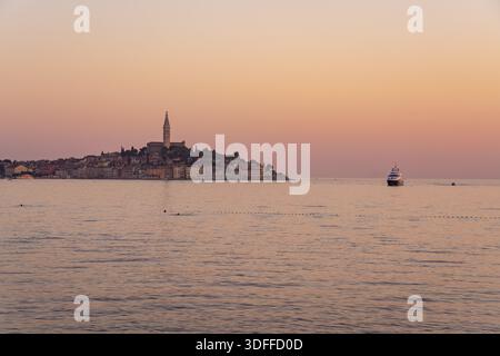 Vista della penisola della città vecchia sotto un cielo morbido e pastello, con la torre della chiesa che si staglia contro l'orizzonte, e dolci onde che riflettono il tramonto Foto Stock