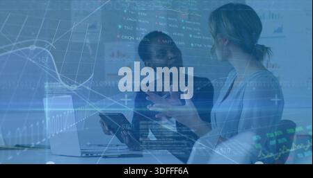 Discutere di due colleghi in blazer che utilizzano tablet in una sala riunioni con notebook, grafici e sovrapposizioni Foto Stock