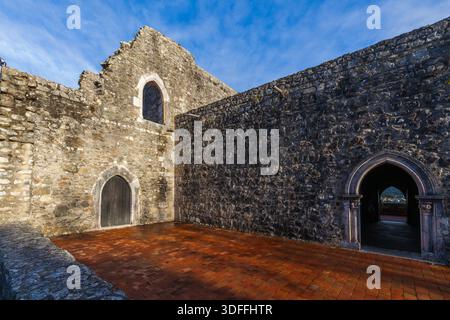 Leiria. L'interno illuminato dal sole di un'antica rovina in pietra presenta massicce pareti, porte ad arco, una porta di legno scuro e un caldo pavimento in piastrelle di terracotta, al Foto Stock