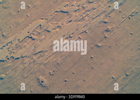 Cattura aerea cinematografica di aridi terreni desertici illuminati dalla luce del tramonto, rivelando intricate crepe e dune di sabbia ruvida. La struttura dorata della terra ricorda un paesaggio marziano o un letto di lago asciutto per l'uso sullo sfondo Foto Stock