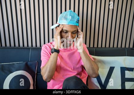 Uomo che tiene la testa soffre di dolore, stress o tensione mentre è seduto al chiuso Foto Stock