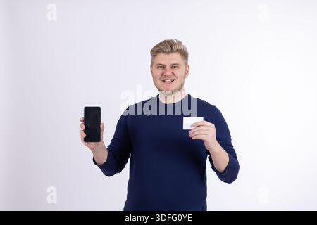 Uomo sorridente in maglione blu con smartphone nero Foto Stock