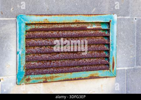 Griglia di ventilazione con cornice in turchese ruggine su pareti in piastrelle grigie, texture industriali e decadimento Foto Stock