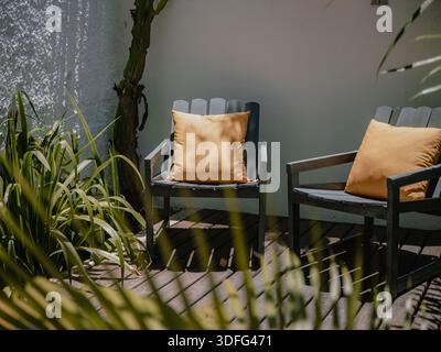 Primo piano di sedie da patio vuote con cuscini alla luce del sole e all'ombra su una terrazza tranquilla. Foto Stock