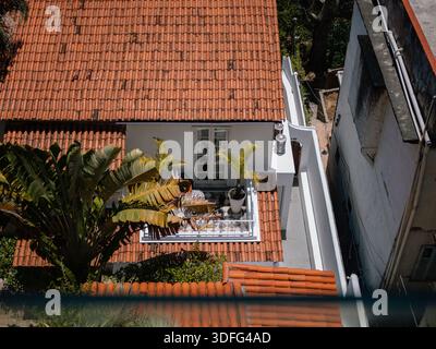 Terrazza sul tetto con tetto in piastrelle rosse, posti a sedere nel patio e piante tropicali alla luce del sole. Foto Stock