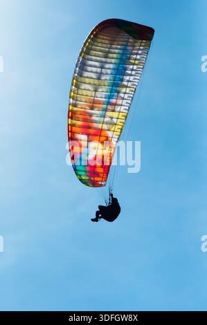 Un parapendio si libra attraverso un cielo blu limpido, con la sua ala colorata che cattura la luce del sole. Foto Stock