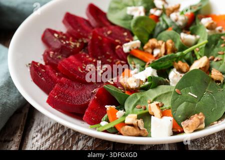 Deliziosa insalata con barbabietole, spinaci, formaggio, noci e carote su tavola di legno, primo piano Foto Stock
