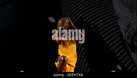 Giocatore di pallacanestro che salta in volo in studio, indossa una maglia gialla e pantaloncini corti Foto Stock