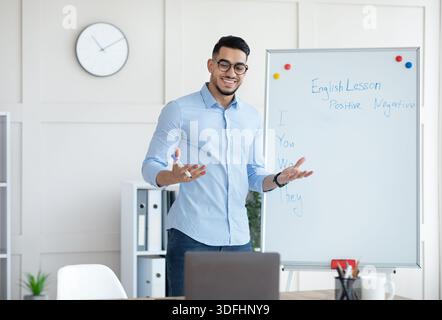 Allegro giovane insegnante arabo in piedi vicino a lavagna e spiegare la grammatica inglese agli studenti online da casa Foto Stock