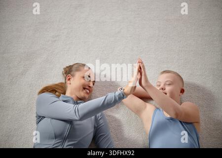 Donna e bambino con sindrome di Down sdraiato sorridente e alto Fiving Foto Stock