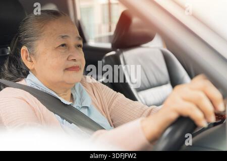 Donna asiatica anziana che guida un'auto con cintura di sicurezza allacciata, consapevolezza della sicurezza per anziani. Messa a fuoco selettiva. Donna anziana che guida un'auto. Foto Stock
