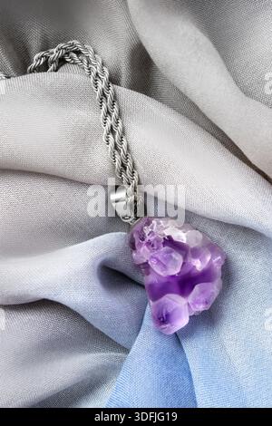 Ciondolo in cristallo ametista su catena argentata adagiata su tessuto in chiffon drappeggiato Foto Stock