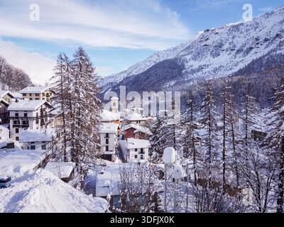 Vista aerea dei tetti innevati e dei pini torreggianti sotto lo sguardo vigile delle lontane montagne innevate, Balme, Piemonte, Italia. Foto Stock