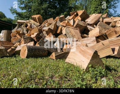 Una grande pila di tronchi di legna da ardere tritati impilati liberamente e appoggiati sull'erba verde in un ambiente naturale all'aperto Foto Stock