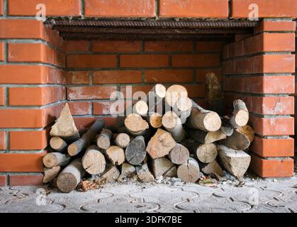 Tronchi di legna da ardere ben impilati in una nicchia all'aperto fatta di mattoni rossi, che mostra texture di legno naturale e fascino rustico all'aperto Foto Stock