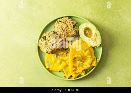 Una variopinta colazione a buffet con uova strapazzate mescolate con rabarbaro, pancake di quinoa e avocado a fette condito con olio d'oliva, il tutto servito su un piatto verde. Foto Stock