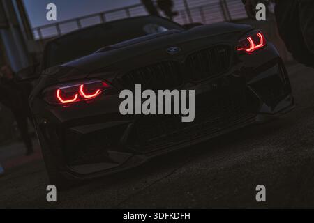 Imola, italia 01 gennaio 2026: bmw m2 performance coupé parcheggiata al crepuscolo, corpo nero e fari rossi accesi che tagliano l'atmosfera urbana del crepuscolo Foto Stock