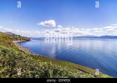 Cielo blu con nuvole bianche e soffici sulla costa rocciosa e montagne in lontananza Foto Stock
