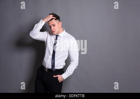 Uomo in camicia bianca e cravatta in posa su sfondo grigio in ambientazione Studio Foto Stock