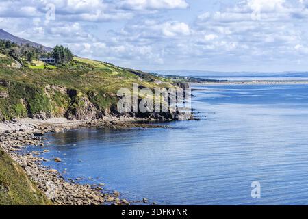 Cielo blu con nuvole bianche e soffici sulla costa rocciosa e montagne in lontananza Foto Stock