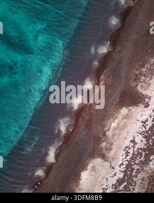 Vista aerea della spiaggia di sabbia scura che incontra il mare turchese cristallino, creando un netto contrasto di texture e toni, Santorini, Grecia. Foto Stock