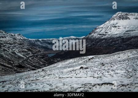 La vista delle montagne innevate sotto un cielo nuvoloso crea un forte contrasto, evocando un senso di serena desolazione a Seydisfjordur, fiordi orientali, Islanda Foto Stock