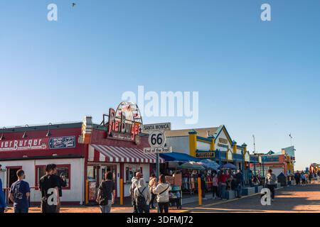 Molo di Santa Monica in California con caffè, ristoranti e turisti, con l'iconico cartello che segna la fine della Route 66. Vivace scena costiera Foto Stock