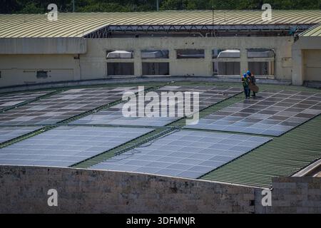 Vista di due lavoratori che installano nuovi pannelli solari su un tetto al caldo sole, creando un contrasto tra il tetto verde e i pannelli lucidi, ca Foto Stock