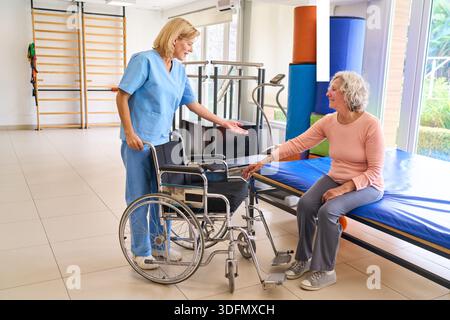 Una donna anziana è assistita da un fisioterapista presso un centro di riabilitazione che utilizza una sedia a rotelle per la mobilità e il recupero dopo una lesione l'immagine mostra Foto Stock