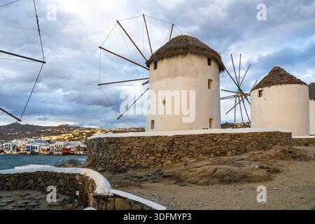 La vista degli iconici mulini a vento si erge orgogliosamente contro il Mar Egeo, affacciato sugli edifici colorati di Mykonos sotto un cielo spettacolare, Mykonos, Mykonos, G. Foto Stock