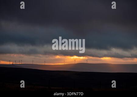 West Yorkshire, Regno Unito. 13 gennaio 2026. Halifax, West Yorkshire, Regno Unito. Tempo Regno Unito il sole tramonta sopra la valle di Calder con la sagoma di turbine eoliche lontane sulla linea aerea e il profilo del monumento Stoodley Pike si trova in alto sulle brughiere Pennine sopra Hebden Bridge, West Yorkshire, Regno Unito . La fotografia è stata scattata da Ovenden Moor, Halifax, West Yorkshire. Crediti: Immagini di mulini a vento/Alamy Live News Foto Stock
